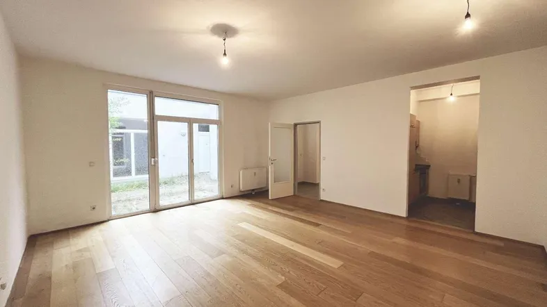 Helles Wohnzimmer mit Holzboden und großzügigem Zugang zu einem kleinen Außenbereich.
