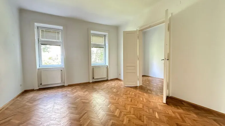Helles Zimmer mit Fischgrätparkettboden, weißen Wänden und zwei Fenstern.