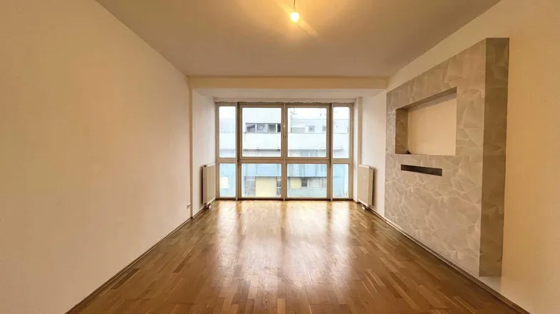Helles Wohnzimmer mit Parkettboden, großen Fenstern und einer modernen Wandgestaltung.