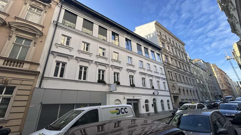 Historisches Gebäude mit klassischer Fassade an einer belebten Stadtstraße mit parkenden Autos.