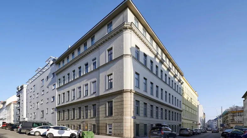 Eckgebäude in städtischer Umgebung mit klassischer Architektur und vielen Fenstern.
