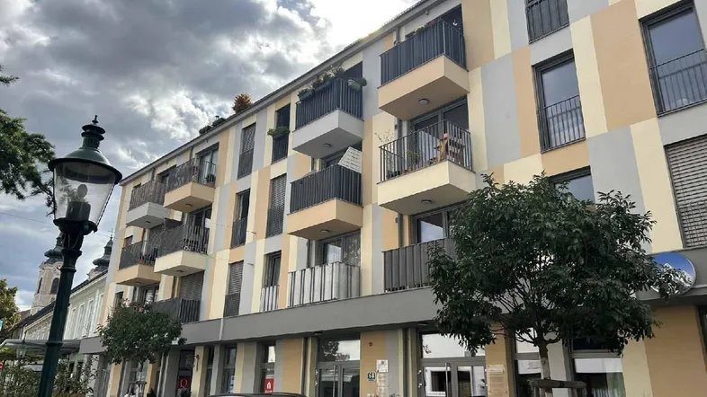 Modernes Mehrfamilienhaus mit Balkonen und farbiger Fassade unter bewölktem Himmel.
