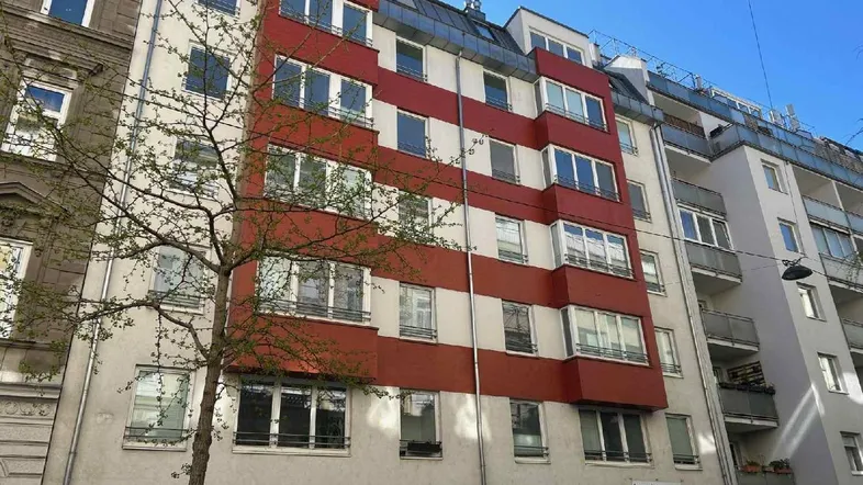 Mehrstöckiges Wohngebäude mit markanter rot-weißer Fassade und großen Fenstern in urbaner Umgebung.
