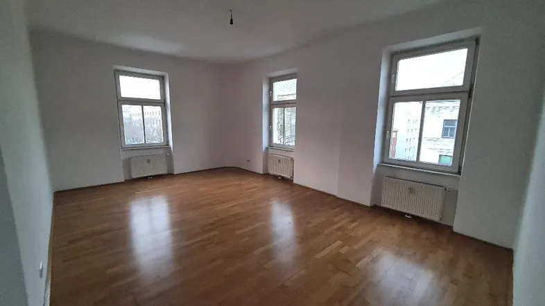Heller, leerer Raum mit Parkettboden und drei Fenstern, ideal als Wohnzimmer.