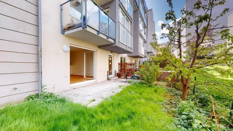 Grüner Gartenbereich mit Rasenfläche und Terrasse vor der Wohnanlage.