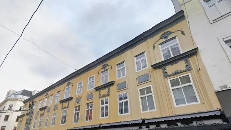 Historisches Gebäude mit gelber Fassade und verzierten Fenstern in städtischer Umgebung.