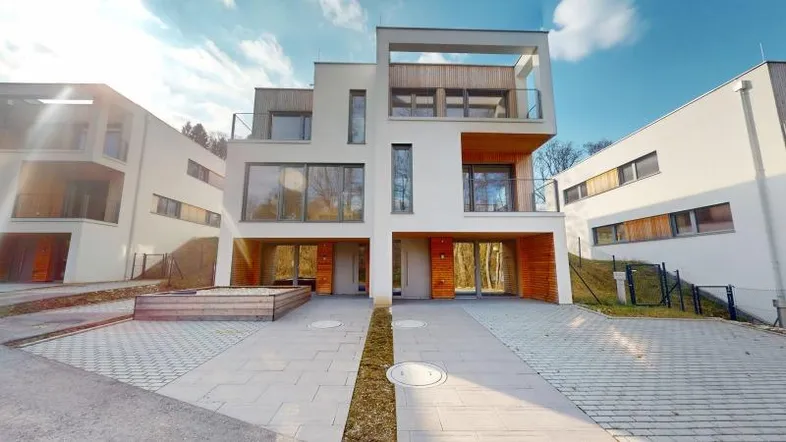 Moderne Reihenhäuser mit weißer Fassade, Holzverkleidung und gepflasterten Zufahrten unter blauem Himmel.