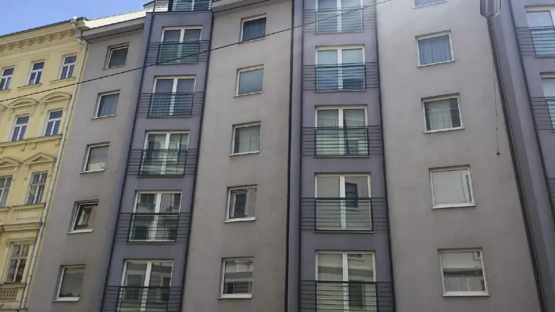 Mehrstöckiges Wohngebäude mit grauer Fassade und Balkonen in städtischer Umgebung.