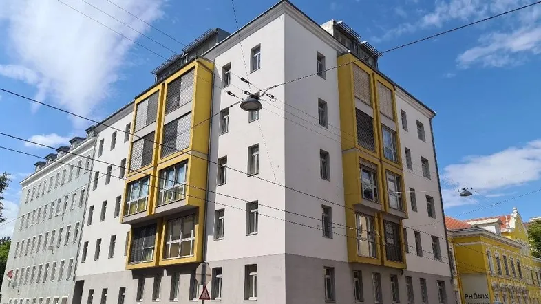 Modernes Wohngebäude mit gelben Akzenten und vielen Fenstern unter blauem Himmel.