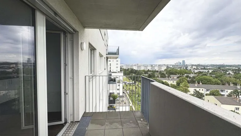 Geräumiger Balkon mit Fliesenboden und weitem Blick über die Stadtlandschaft unter bewölktem Himmel.