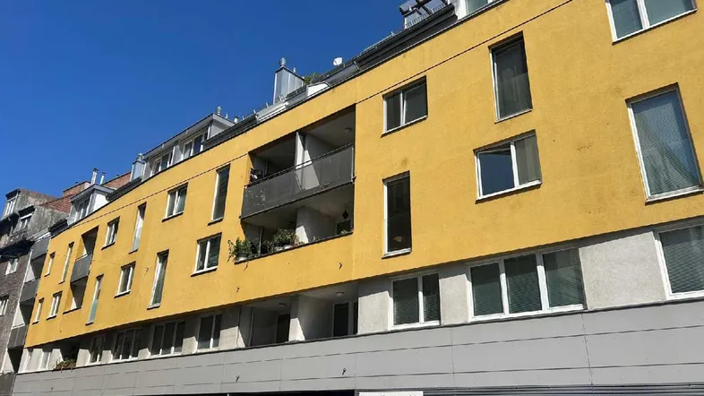 Gelbe Fassade eines modernen Wohngebäudes mit Balkonen und vielen Fenstern.