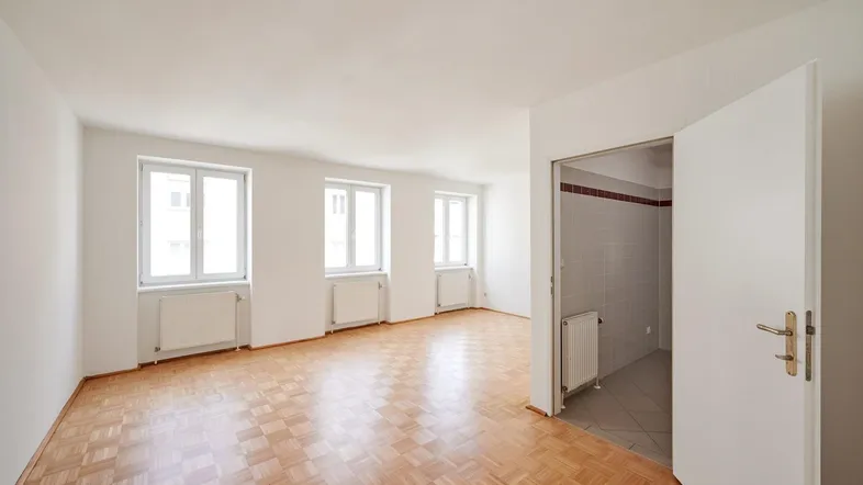 Helles, leeres Zimmer mit Parkettboden und mehreren Fenstern, bereit zur individuellen Gestaltung.