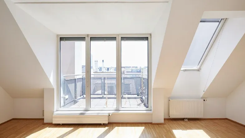 Helles Dachgeschosszimmer mit Holzboden, großen Fenstern und Zugang zu einer Dachterrasse.