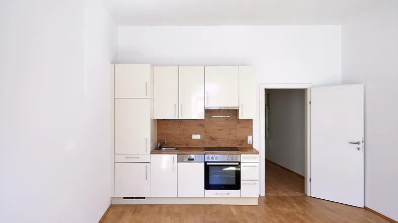 Kleine, moderne Einbauküche mit weißen Schränken, Holzarbeitsplatte und integrierten Geräten.