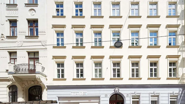 Klassische Fassade eines Mehrfamilienhauses mit vielen Fenstern und einem Balkon im ersten Stock.