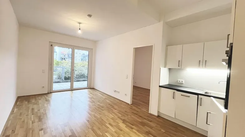 Helles Wohnzimmer mit Parkettboden, Zugang zur Terrasse und integrierter Küchenzeile.