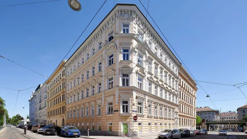 Historisches Eckgebäude mit klassischer Fassade und vielen Fenstern in städtischer Umgebung.