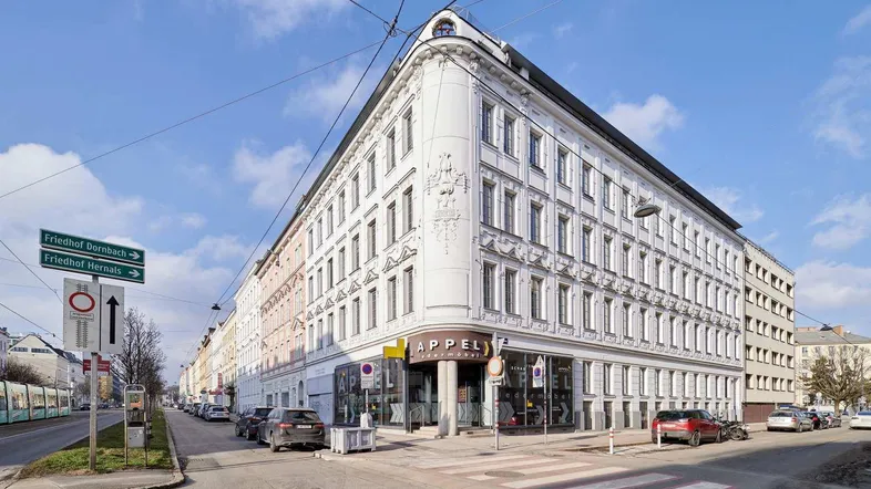Eckgebäude mit klassischer Architektur und Geschäftsflächen im Erdgeschoss an einer belebten Straße.