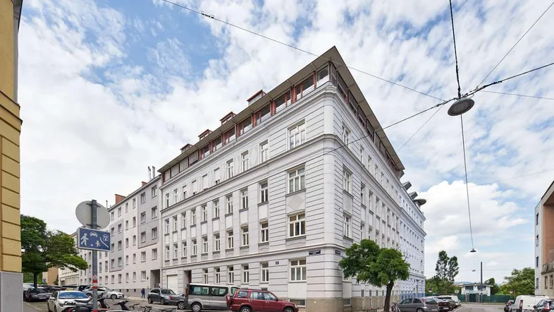 Eckgebäude mit klassischer Fassade und Dachausbau in städtischer Umgebung.