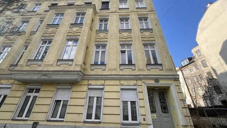 Vorderansicht eines historischen Mehrfamilienhauses mit gelber Fassade und vielen Fenstern.