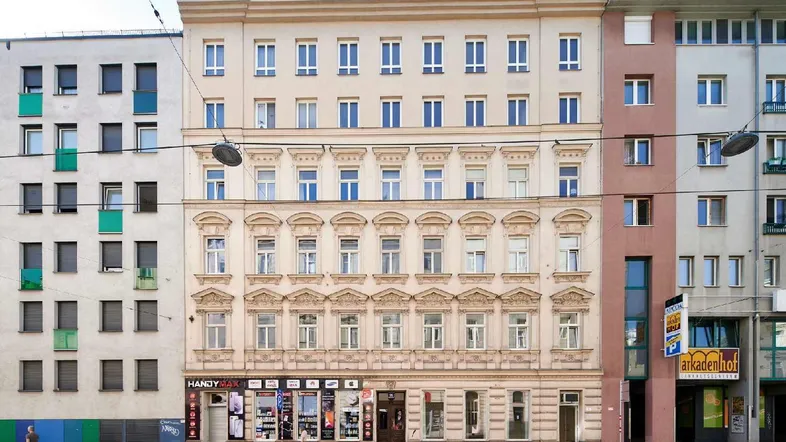 Ansicht der Straßenfassade eines Mehrfamilienhauses mit Geschäften im Erdgeschoss und Wohnungen darüber.