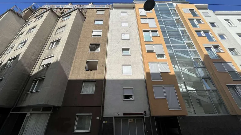 Moderne Gebäudefassade mit großen Fenstern und einem markanten Glasanbau unter blauem Himmel.