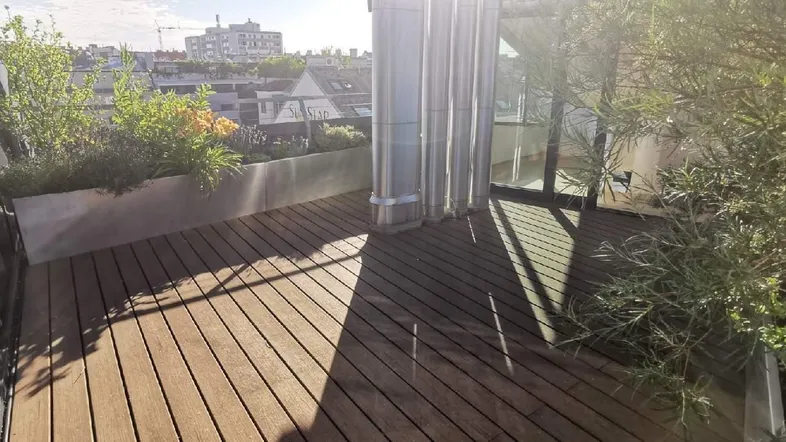 Geräumige Dachterrasse mit Holzbelag und Pflanzen, bietet einen schönen Blick über die Stadt.