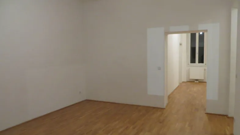 Helles, leeres Zimmer mit Parkettboden und Zugang zu einem weiteren Raum.