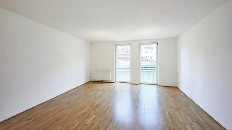 Helles Zimmer mit Parkettboden und Zugang zu einem französischen Balkon.