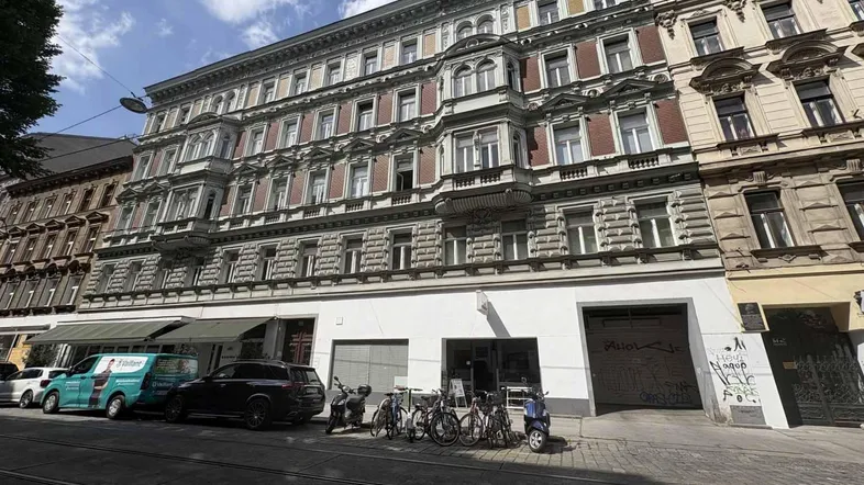 Fassade eines historischen Mehrfamilienhauses an einer belebten Straße mit Geschäften im Erdgeschoss.