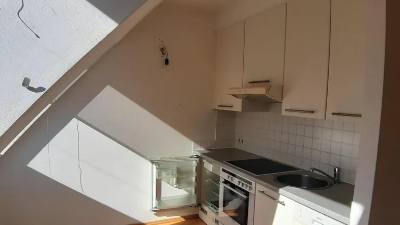 Helle Dachgeschossküche mit Einbaugeräten, weißen Schränken und Holzfußboden, durchflutet von Sonnenlicht.