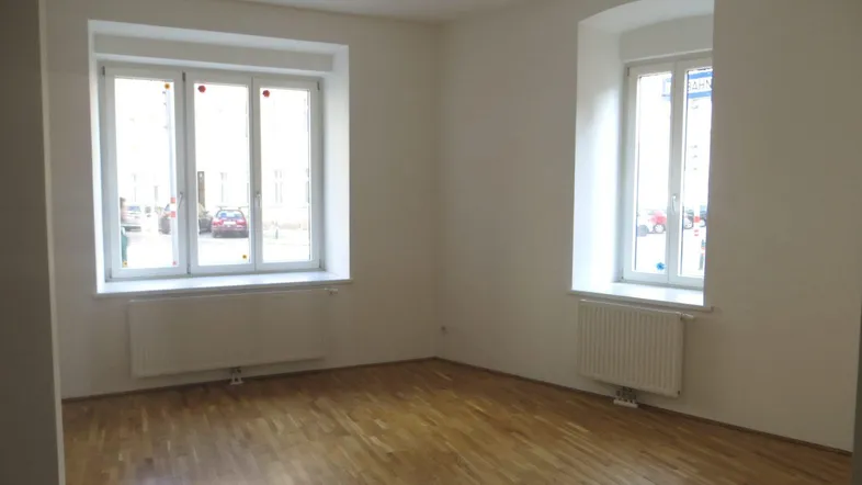 Helles Zimmer mit Parkettboden und zwei Fenstern, ideal als Wohn- oder Schlafzimmer nutzbar.