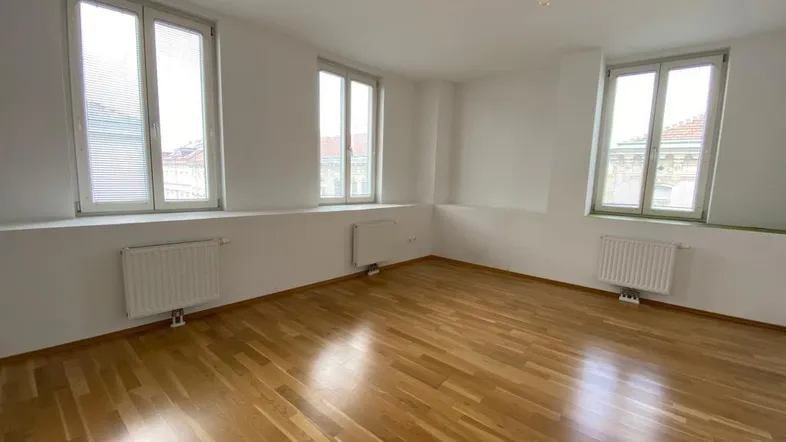 Helles, leeres Zimmer mit Parkettboden und mehreren Fenstern, bereit zur individuellen Gestaltung.