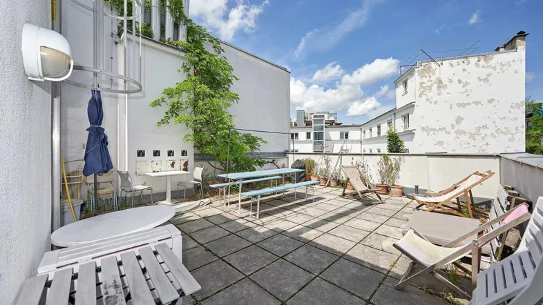 Geräumige Dachterrasse mit Sitzgelegenheiten und Liegestühlen unter blauem Himmel.