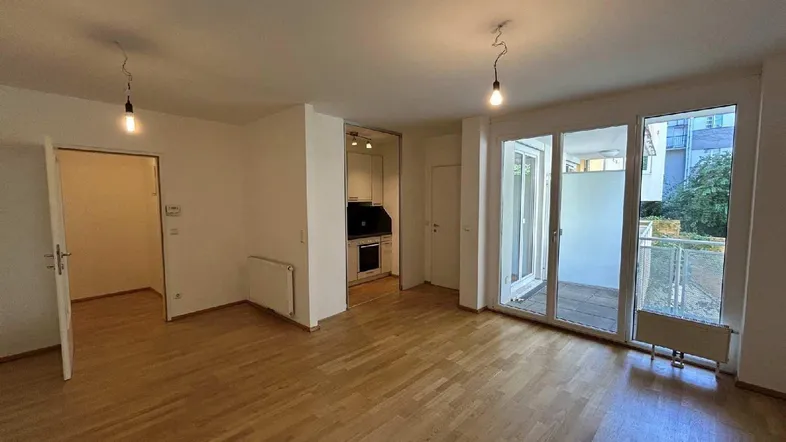 Heller Wohnbereich mit Parkettboden, integrierter Küchenzeile und Zugang zum Balkon.