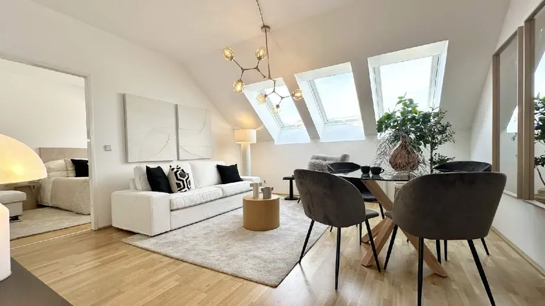 Helles Wohn- und Esszimmer mit Dachfenstern, Holzboden und Zugang zu einem Schlafzimmer.