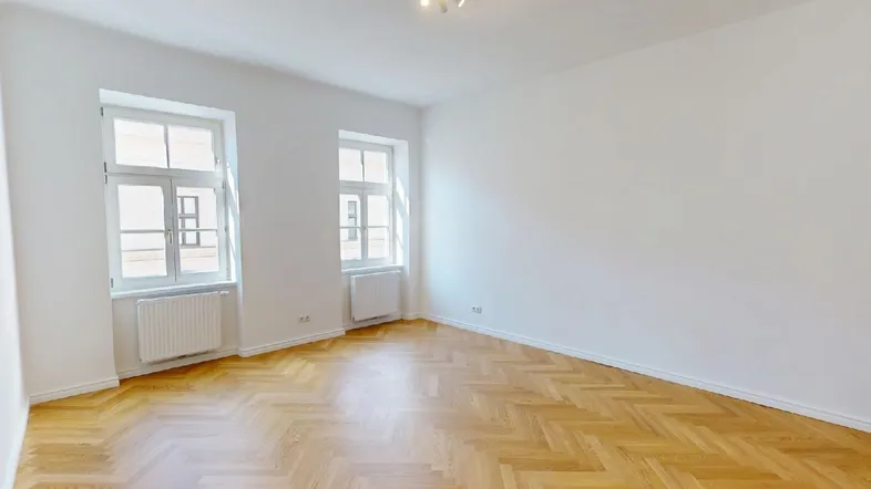 Helles Zimmer mit Fischgrätparkettboden und zwei großen Fenstern, ideal als Wohn- oder Schlafzimmer.