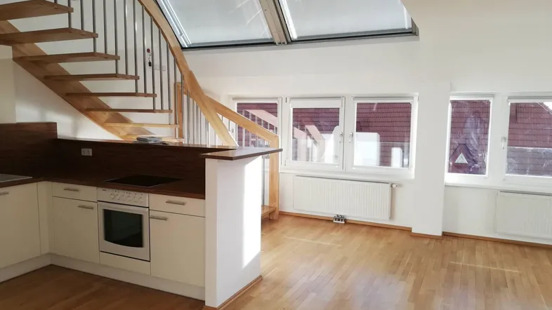 Heller offener Wohnbereich mit integrierter Küche, Holztreppe und großen Fenstern sowie Dachfenstern.