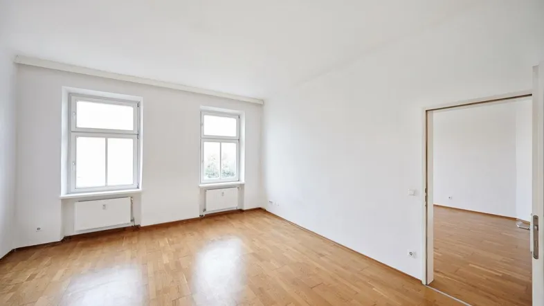 Geräumiges Zimmer mit klassischem Parkettboden und einem offenen Durchgang zu einem weiteren Raum.