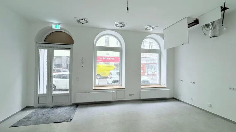 Heller, leerer Geschäftsraum mit großen Bogenfenstern, modernen Lüftungsschlitzen und frisch gestrichenen Wänden.