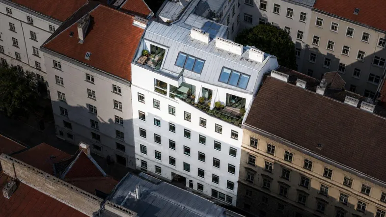 Luftaufnahme eines Stadtblocks mit verschiedenen Gebäuden, darunter ein modernes mit Dachterrassen.