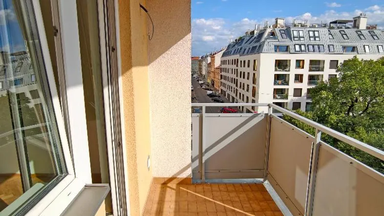Heller Balkon mit Terrakotta-Fliesenboden und Blick auf die Stadt und umliegende Gebäude.