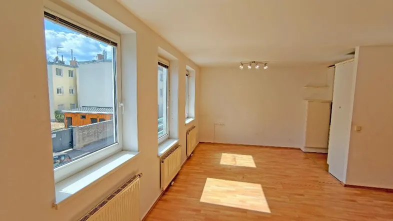 Helles, leeres Wohnzimmer mit Holzfußboden und Blick auf den Innenhof.