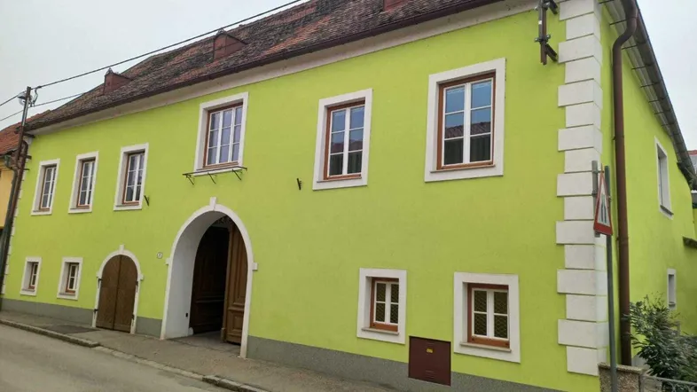 Traditionelles Gebäude mit leuchtend grüner Fassade und roten Ziegeldächern an einer ruhigen Straße gelegen.