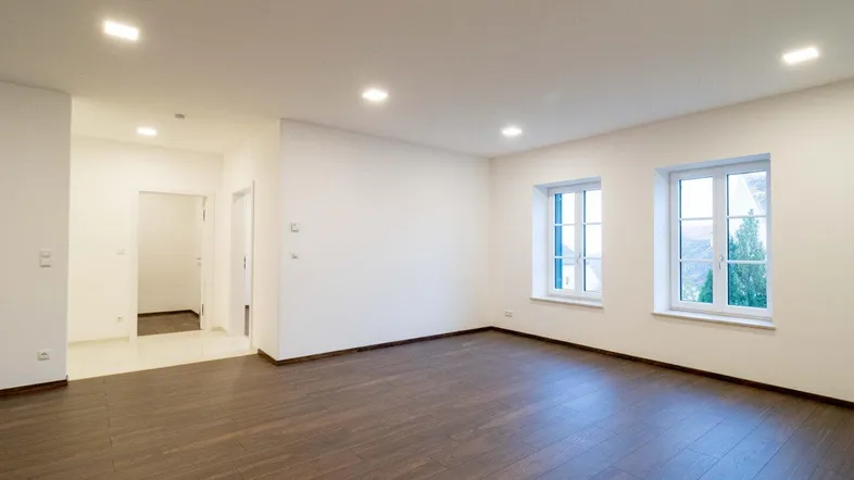 Geräumiger, heller Raum mit dunklem Holzboden und Einbaustrahlern, ideal als Wohnzimmer nutzbar.