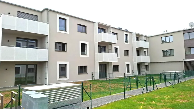 Seitenansicht eines Neubaus mit modernen Balkonen und kleinen Gartenbereichen im Erdgeschoss.