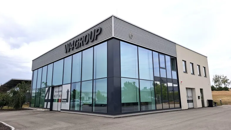 Modernes Geschäftsgebäude mit großer Glasfassade und markanter Beschriftung, umgeben von einem Parkplatz.