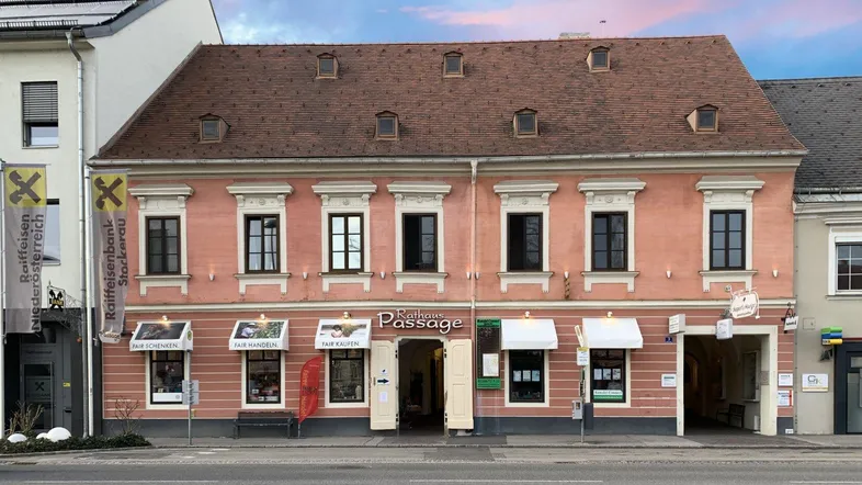 Historisches Gebäude mit rosa Fassade und Geschäften im Erdgeschoss unter einem dramatischen Himmel.