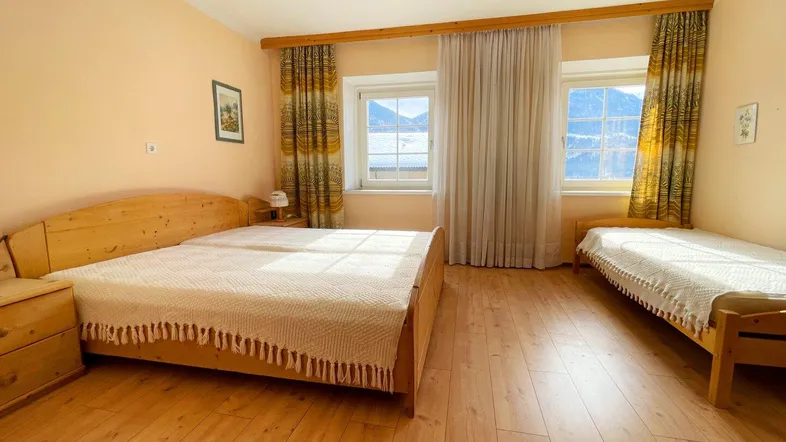 Gemütliches Schlafzimmer mit zwei Holzbetten, Parkettboden und malerischem Bergblick aus den Fenstern.