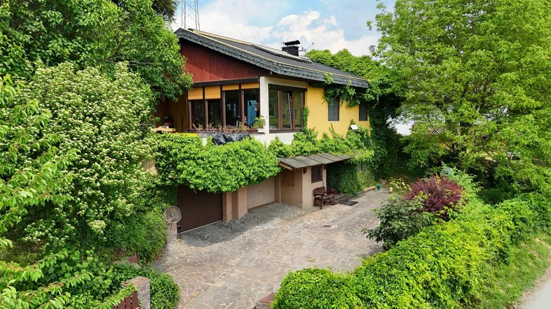 Haus mit gelber Fassade, umgeben von üppigem Grün und einer gepflasterten Auffahrt.